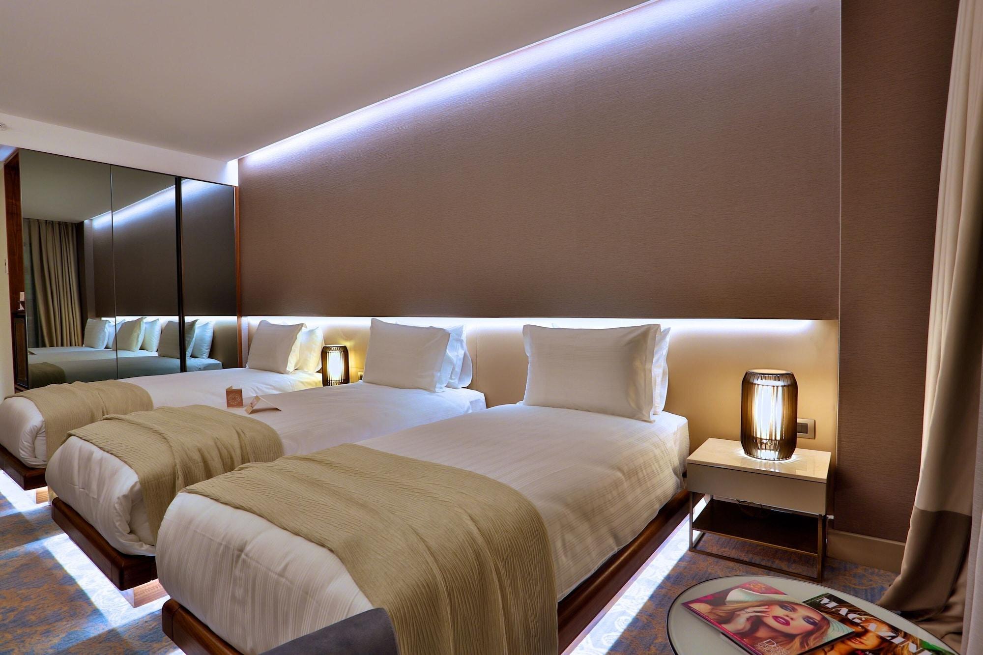 Dosso Dossi Hotels & Spa Downtown Estambul Exterior foto The photo shows a modern hotel room with two neatly made beds. Each bed is dressed with white linens and has a light-colored throw blanket. There are stylish bedside lamps on either side of the beds, as well as small nightstands. The wall behind the 