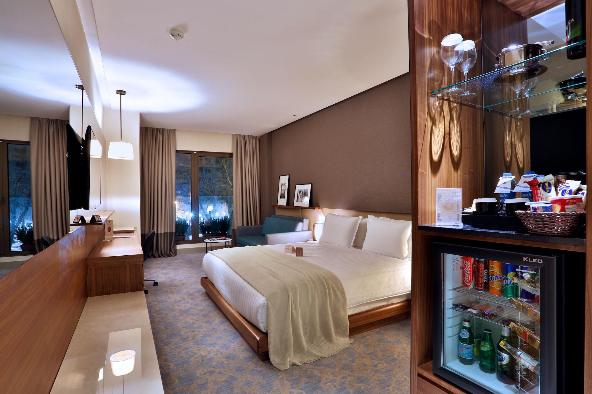 Dosso Dossi Hotels & Spa Downtown Estambul Exterior foto The photo shows a well-decorated hotel room featuring a large bed with white linens, a bedside table, and modern furnishings. There are two windows with curtains that allow natural light to enter the space, and the walls are painted in warm, neutral 