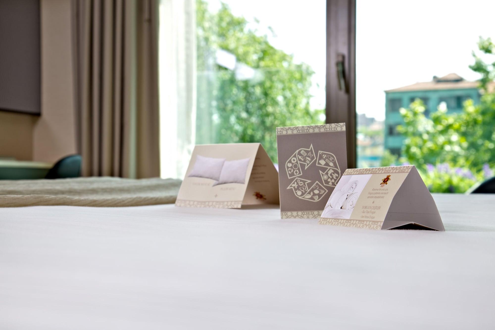 Dosso Dossi Hotels & Spa Downtown Estambul Exterior foto The photo shows a neatly made bed with a soft, white bedspread. In the foreground, there are three triangular cards placed upright on the bed. Each card has different designs or text, with one appearing to feature a pillow image and another possibly 