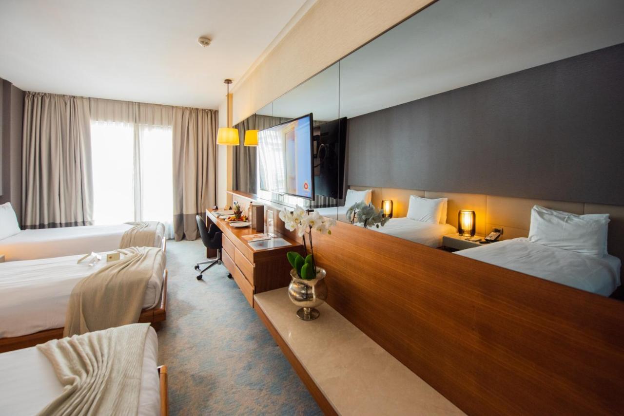 Dosso Dossi Hotels & Spa Downtown Estambul Exterior foto The photo shows a modern hotel room featuring two beds with light-colored bedding. There is a large mirror above a wooden dresser, which holds some decorative items, including a small plant. A TV is mounted on the wall, and there is a workspace with 
