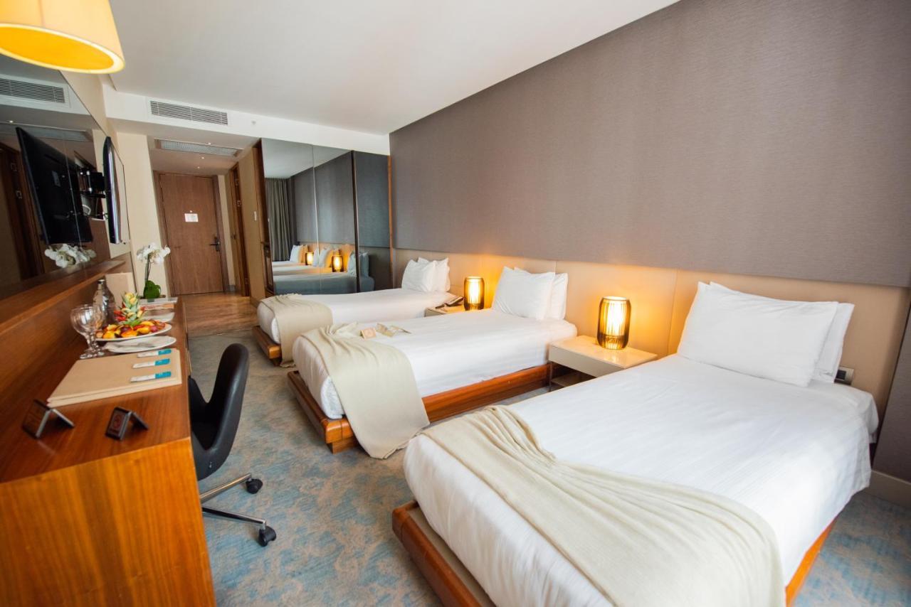 Dosso Dossi Hotels & Spa Downtown Estambul Exterior foto The photo shows a modern hotel room featuring two single beds, each with white linens and a light blanket partially draped over them. There are stylish bedside lamps on either side of the beds, providing a warm glow. A wooden desk and chair are posit