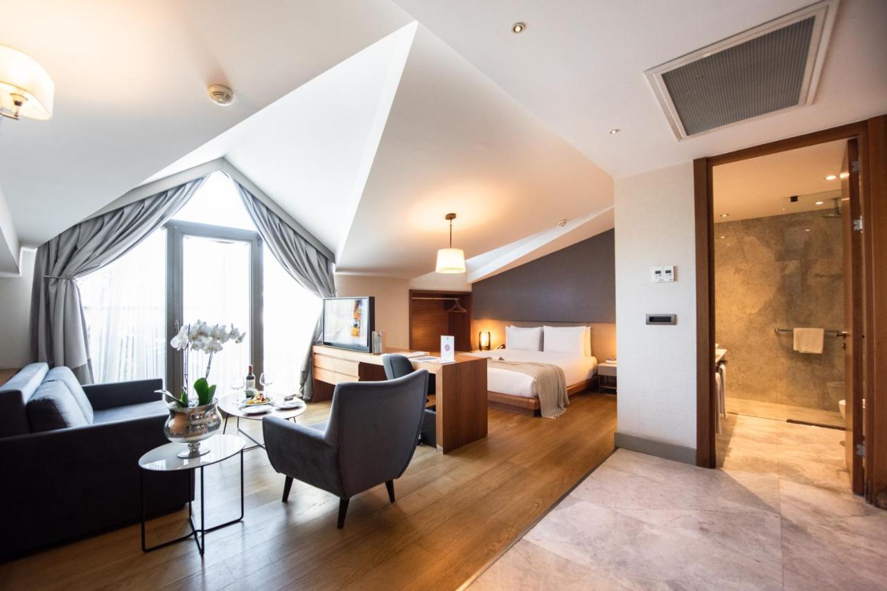 Dosso Dossi Hotels & Spa Downtown Estambul Exterior foto The photo shows a stylish hotel room with a modern design. It features slanted ceilings and large windows that allow natural light to flood the space. The room includes a comfortable seating area with a sofa and a small table, as well as a well-made 