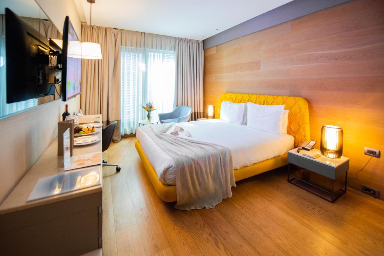 Dosso Dossi Hotels & Spa Downtown Estambul Exterior foto The photo shows a modern hotel room with a cozy and inviting atmosphere. The room features a large bed with a yellow upholstered headboard, topped with white bedding and a soft gray throw blanket casually draped over it. To the side of the bed is a s