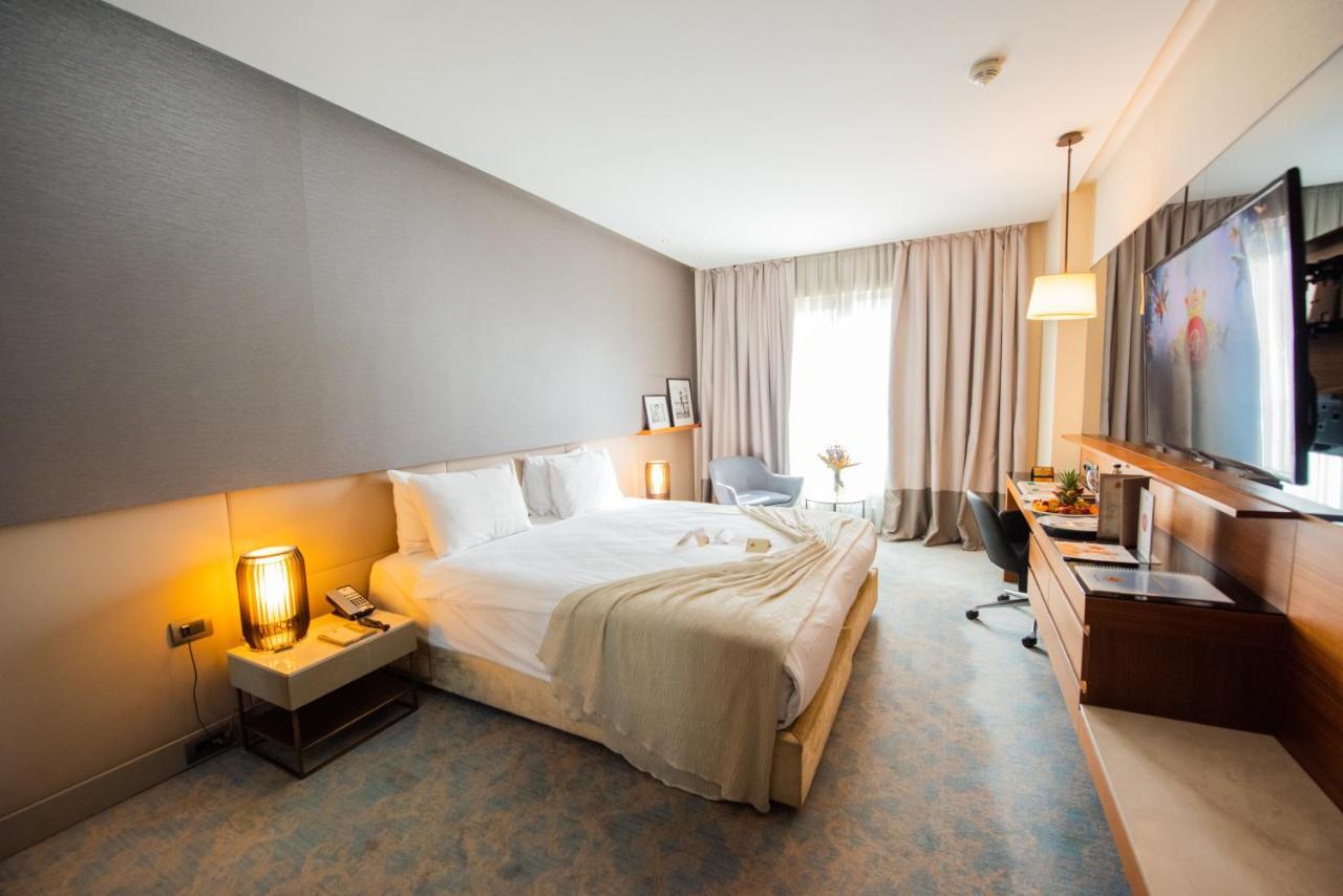 Dosso Dossi Hotels & Spa Downtown Estambul Exterior foto The photo shows a modern hotel room with a comfortable layout. There's a large bed with white linens and a soft throw blanket. Beside the bed, there are bedside tables with lamps. A window covered with sheer curtains allows natural light to enter the