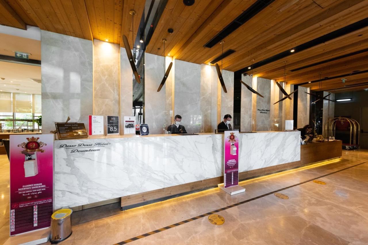 Dosso Dossi Hotels & Spa Downtown Estambul Exterior foto The photo shows a hotel reception area. The front desk is made of elegant marble, and the space features wooden accents on the ceiling. Behind the counter, two staff members are visible, likely assisting guests. There are signs and promotional materi