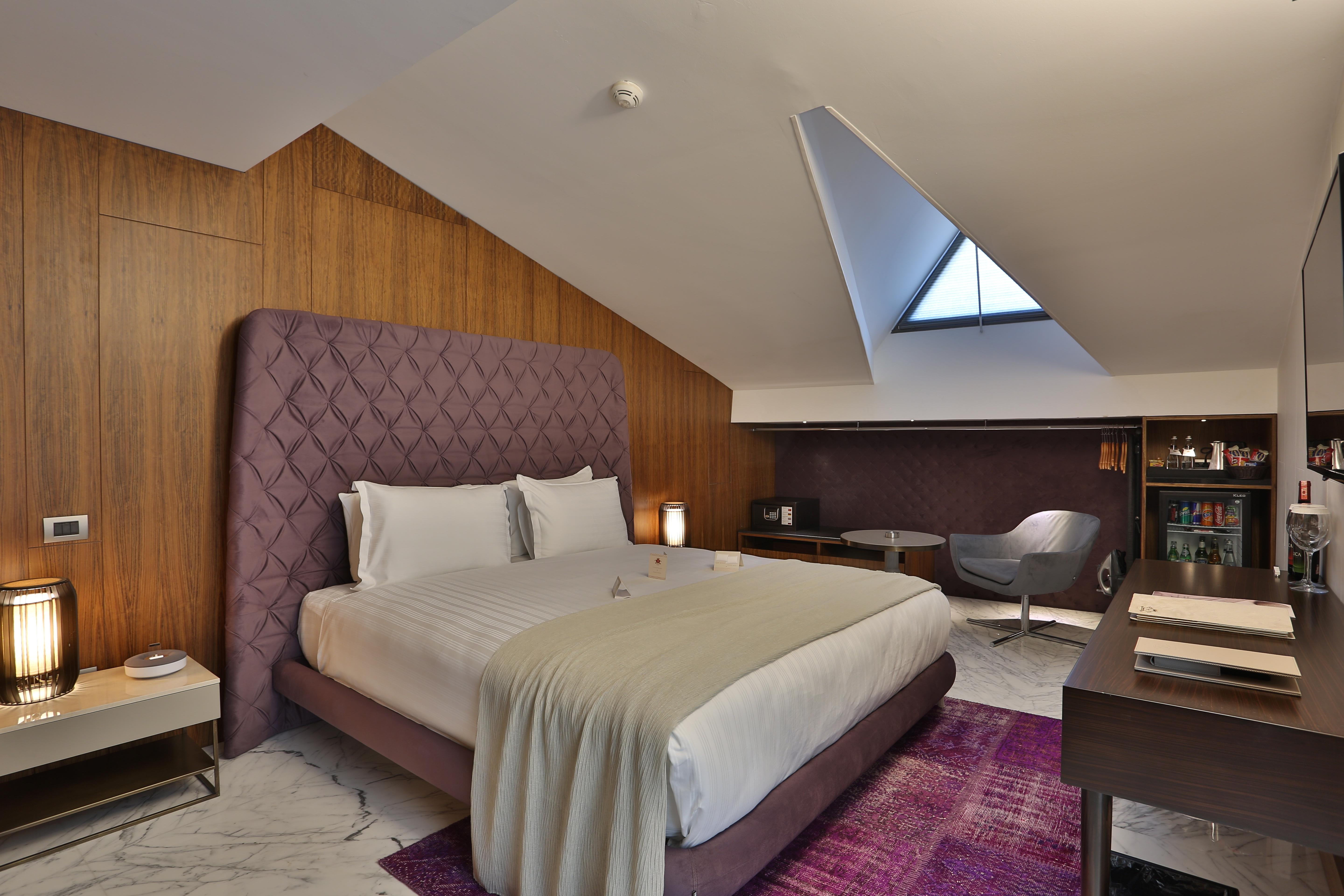 Dosso Dossi Hotels & Spa Downtown Estambul Exterior foto The photo shows a stylish hotel room with a modern design. It features a large bed with a tufted purple headboard, complemented by white bedding and a light gray throw. The walls are made of wooden panels, adding warmth to the space. To the side, the