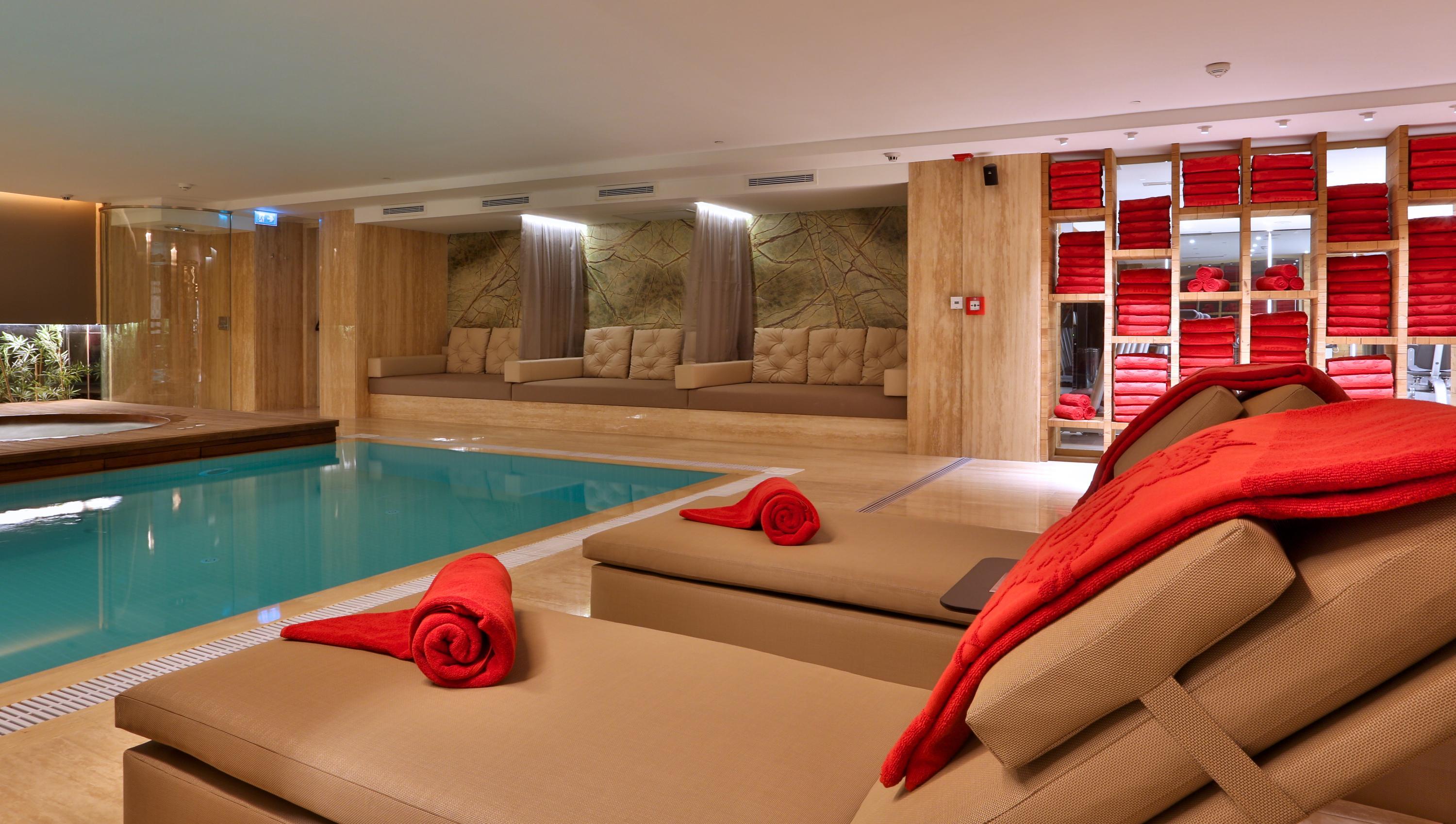 Dosso Dossi Hotels & Spa Downtown Estambul Exterior foto The photo shows a modern, luxurious spa area featuring a swimming pool. In the foreground, there are comfortable lounge chairs with red towels rolled and placed on them. The walls are decorated with wood paneling, and there are several plush seating 