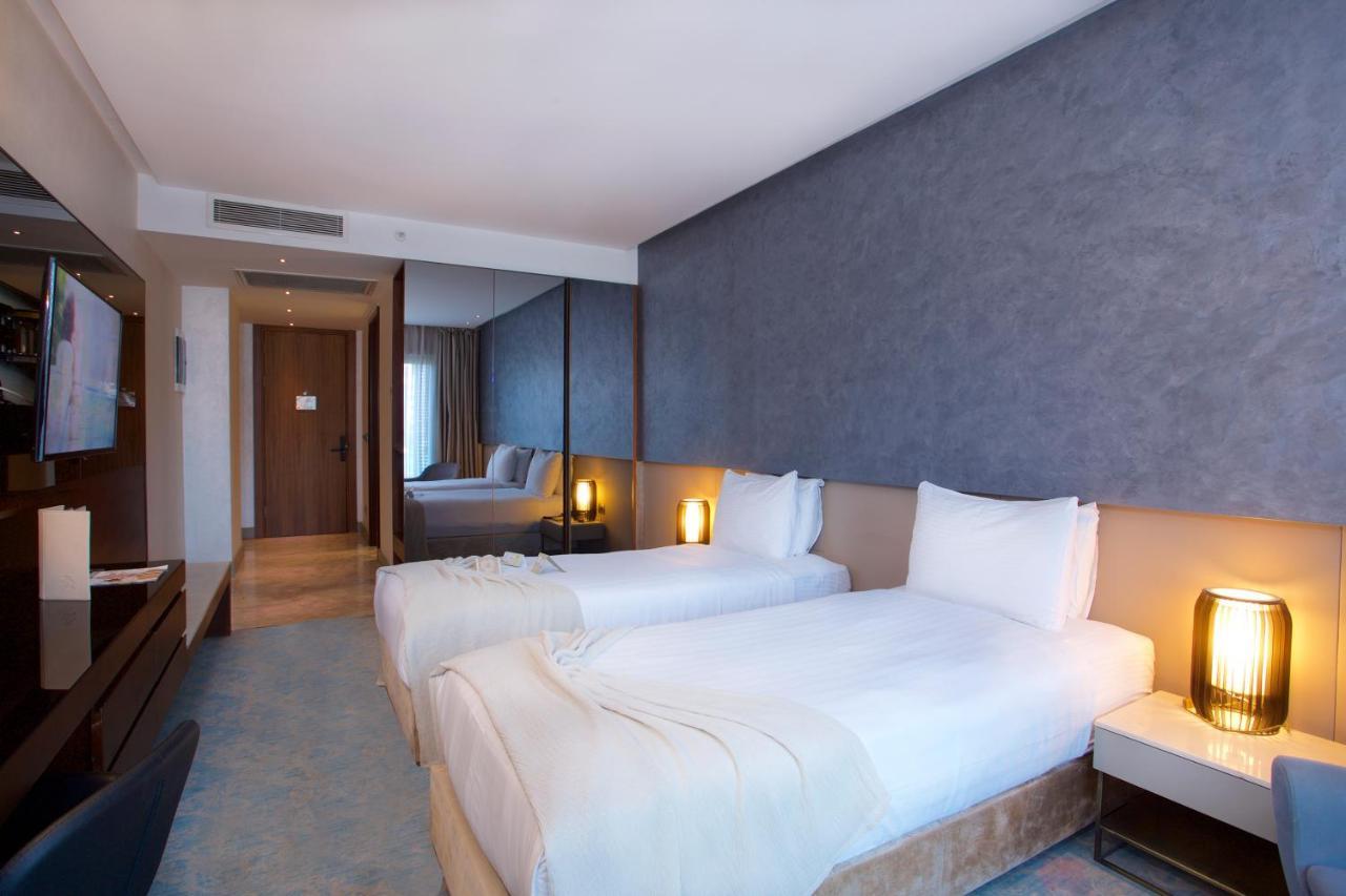 Dosso Dossi Hotels & Spa Downtown Estambul Exterior foto The photo shows a modern hotel room featuring two single beds with white bedding. The walls have a stylish gray finish, and there is a decorative element behind the beds. On either side of the beds, there are bedside tables with lamps. A flat-screen 