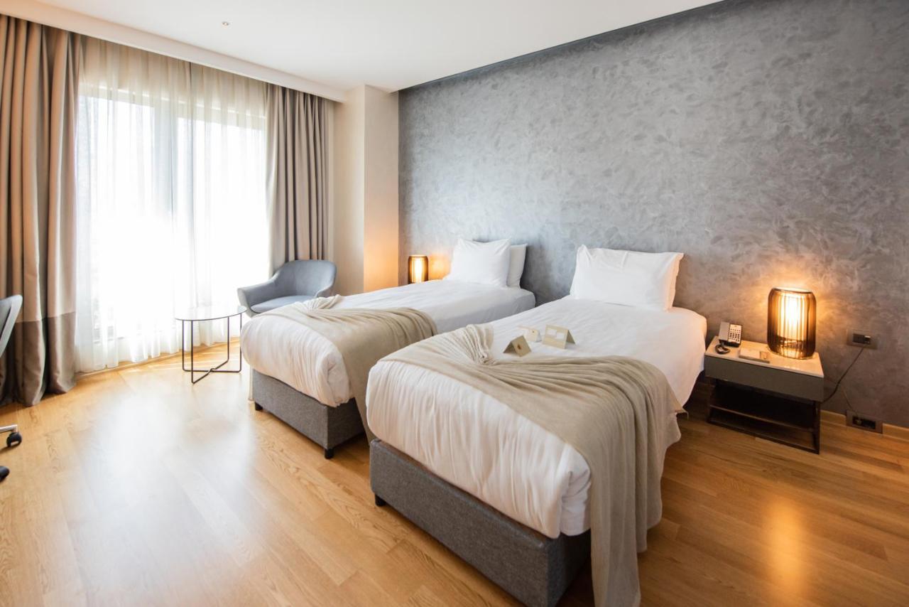 Dosso Dossi Hotels & Spa Downtown Estambul Exterior foto The photo shows a modern hotel room featuring two single beds with white linens and soft gray throw blankets. The room has a stylish design, with wooden flooring and a large window dressed with light curtains that allow natural light to enter. There'