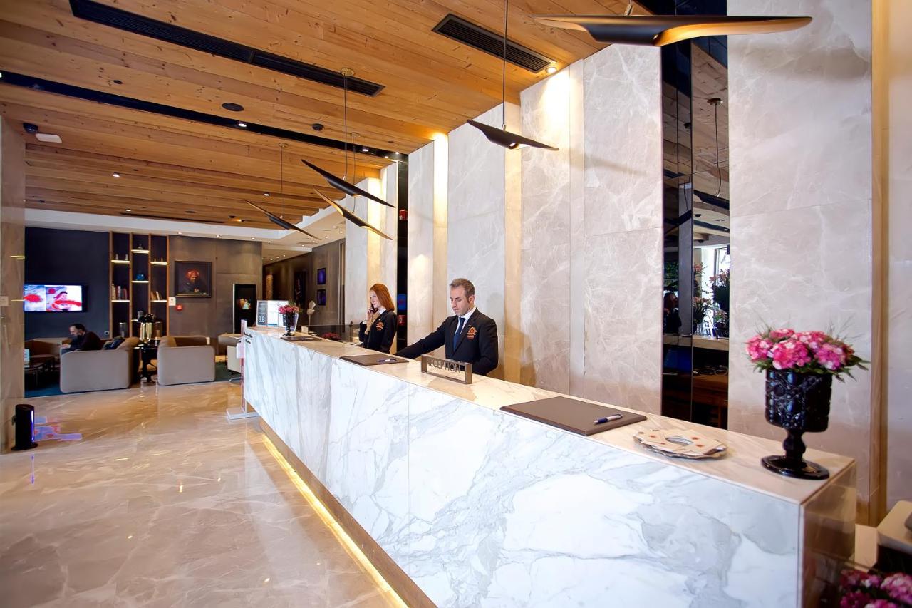 Dosso Dossi Hotels & Spa Downtown Estambul Exterior foto The photo shows a hotel lobby reception area. The reception desk is elegantly designed with a marble surface and is situated against a backdrop of light-colored walls. There are two staff members behind the desk—one is a man in a suit, and the other 