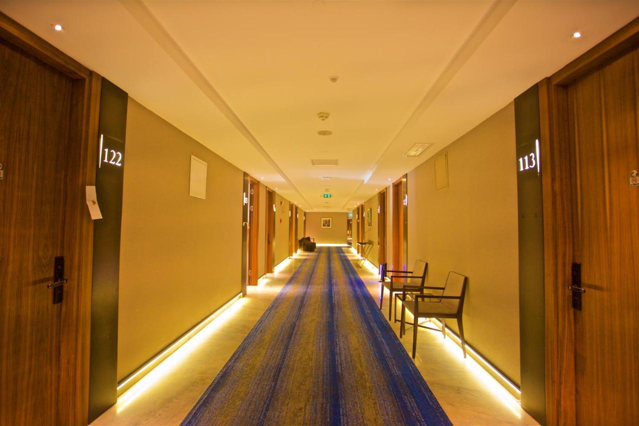 Dosso Dossi Hotels & Spa Downtown Estambul Exterior foto The photo shows a hotel corridor with several wooden doors on either side. Each door is numbered, with numbers visible for rooms 113 and 122. The hallway features a long blue rug running down the center and has soft lighting along the sides, creating