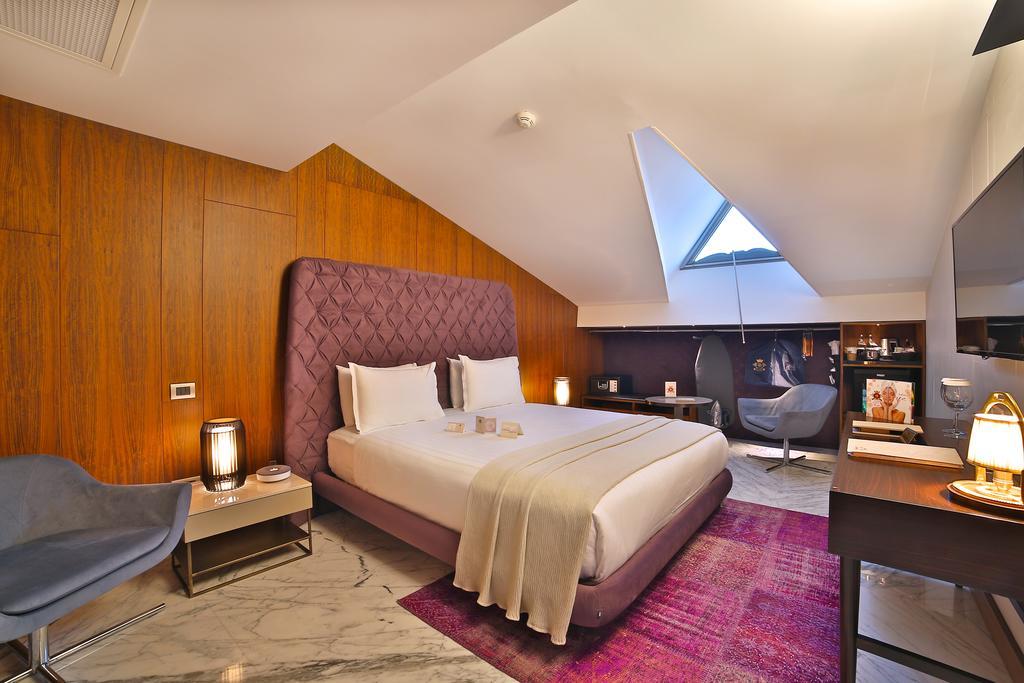Dosso Dossi Hotels & Spa Downtown Estambul Exterior foto The photo shows a modern hotel room featuring a stylish design. It has a large bed with a purple headboard, neatly made with white bedding. The walls are a warm wooden tone, and the room has slanted ceilings with a skylight that lets in natural light